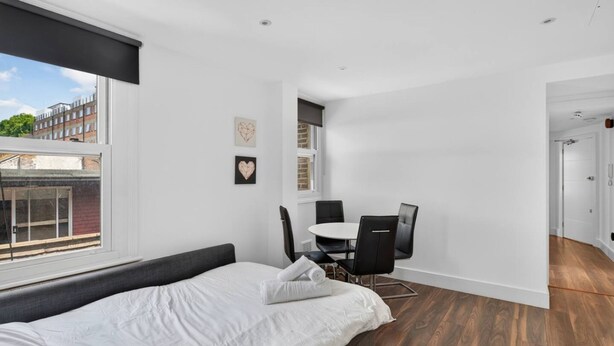 A modern bedroom with a bed, a dining table with chairs, and a view of the outside. - Cool London Flat Spr3 (London)