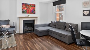 A modern living room with a grey sectional sofa, a fireplace, and a large abstract painting. - Cool London Flat Spr3 (London)