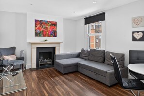 Ein modernes Wohnzimmer mit einem grauen Ecksofa, einem Kamin und einem großen abstrakten Gemälde.