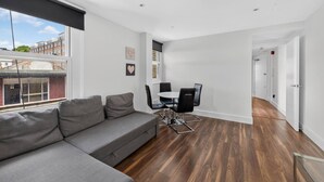 A modern living room with a grey sofa, a dining table with chairs, and a view of the city through large windows. - Cool London Flat Spr3 (London)