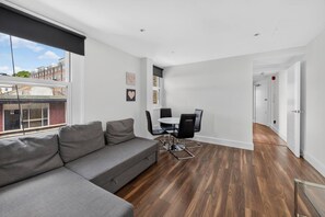 Ein modernes Wohnzimmer mit grauem Sofa, einem Esstisch mit Stühlen und Blick auf die Stadt durch große Fenster.