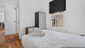 Un dormitorio con cama, armario y ventana que da a una pared de ladrillo y una persona afuera.