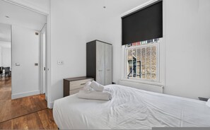 Ein Schlafzimmer mit einem Bett, einem Kleiderschrank und einem Fenster mit Blick auf eine Ziegelwand und eine Person draußen.