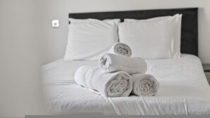 Una cama bien hecha con sábanas blancas y toallas enrolladas.
