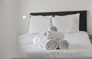 Ein ordentlich bezogenes Bett mit weißen Leinentüchern und aufgerollten Handtüchern.