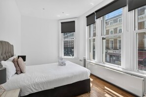 A bedroom with a large bed, a window with a view of buildings, and a radiator. - Trendy London Apartment Spr2 (London)