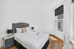 A modern bedroom with a large bed, two bedside tables, a window with a view, and a radiator. - Trendy London Apartment Spr2 (London)