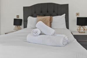 A neatly made bed with a tufted headboard, two white pillows, and a folded towel. - Trendy London Apartment Spr2 (London)