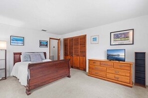Quarto com cama de madeira, cômoda e televisão.