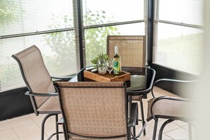 Ein Essbereich mit Tisch und Stühlen, ein Tablett mit Flasche und Gläsern sowie Blick durch große Fenster.