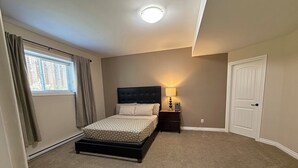 Une chambre à coucher avec un lit, une table de chevet, une lampe, une fenêtre avec des rideaux et une porte.
