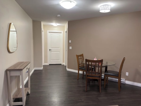 A dining area with a table and chairs, a mirror on the wall, and a door leading to another room.