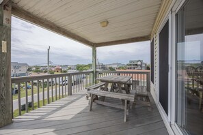 En træterrasse med et bord og stole, et gelænder og udsigt over et boligområde med huse og en vej.