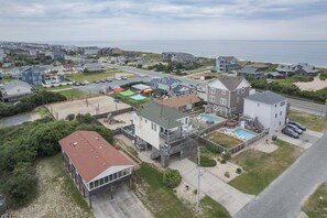 A coastal residential area with houses, a swimming pool, and a beach in the background. - 5433 - Sonnie Beaches Ocean-view 4BR, 4.5BA home with private pool, hot tub, and game room. (Nags Head)