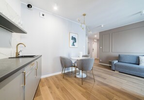 Una cocina moderna con horno integrado, un comedor con una mesa redonda y dos sillas, y una sala de estar con un sofá y un cojín azul.