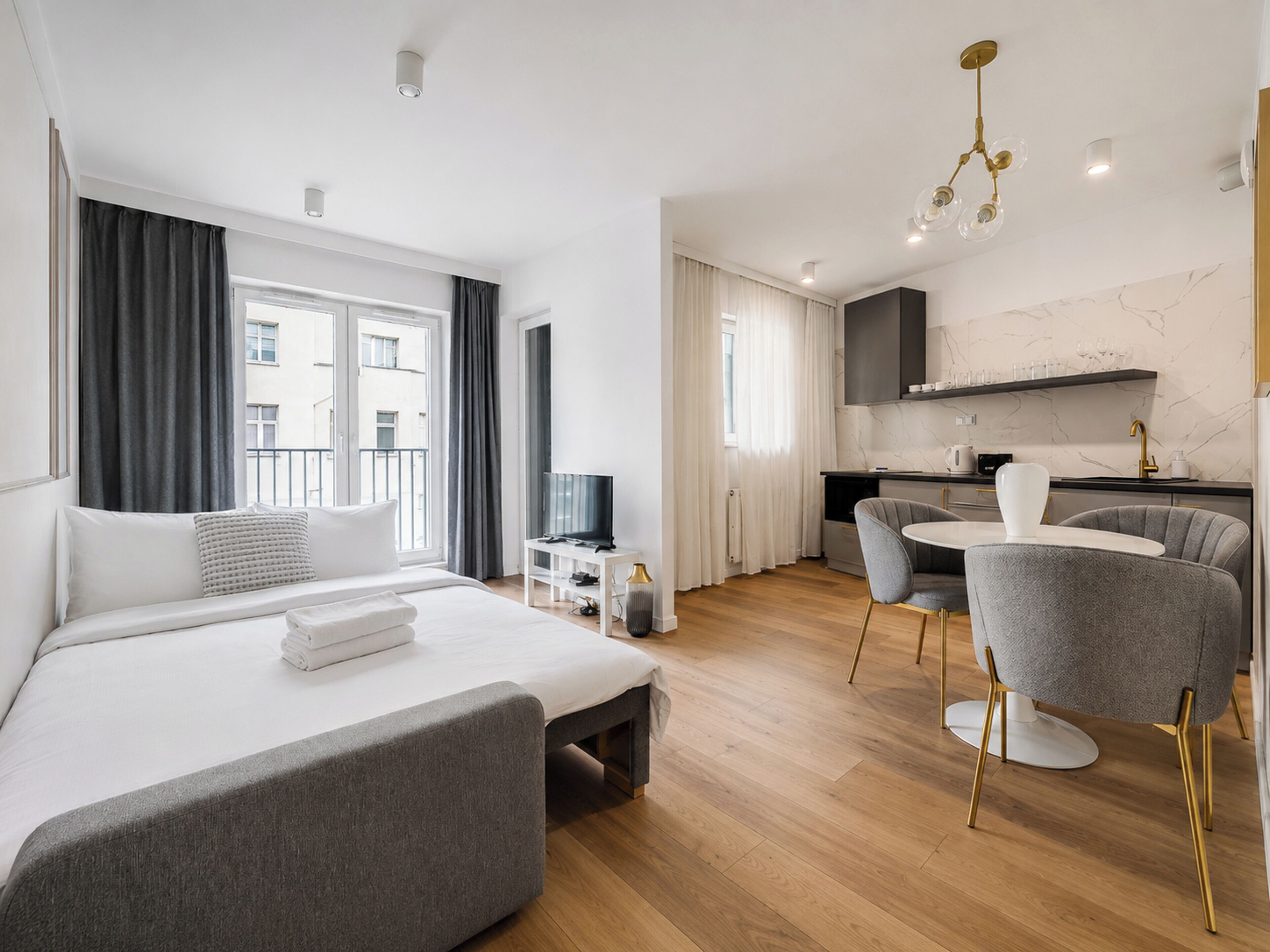 A modern hotel room with a bed, a desk, a chair, and a kitchenette.