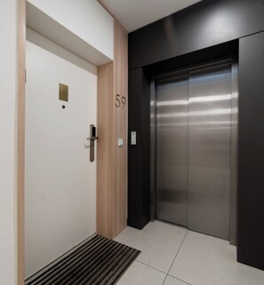 A modern elevator with a metallic finish, a wooden door with a brass plate, and a number '59' on the wall. - Sikorskiego Serene Apartment (Poznań)
