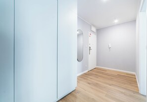 A hallway with a wooden floor, white walls, a door with a red emergency exit sign, and a wall-mounted light fixture. - Sikorskiego Serene Apartment (Poznań)