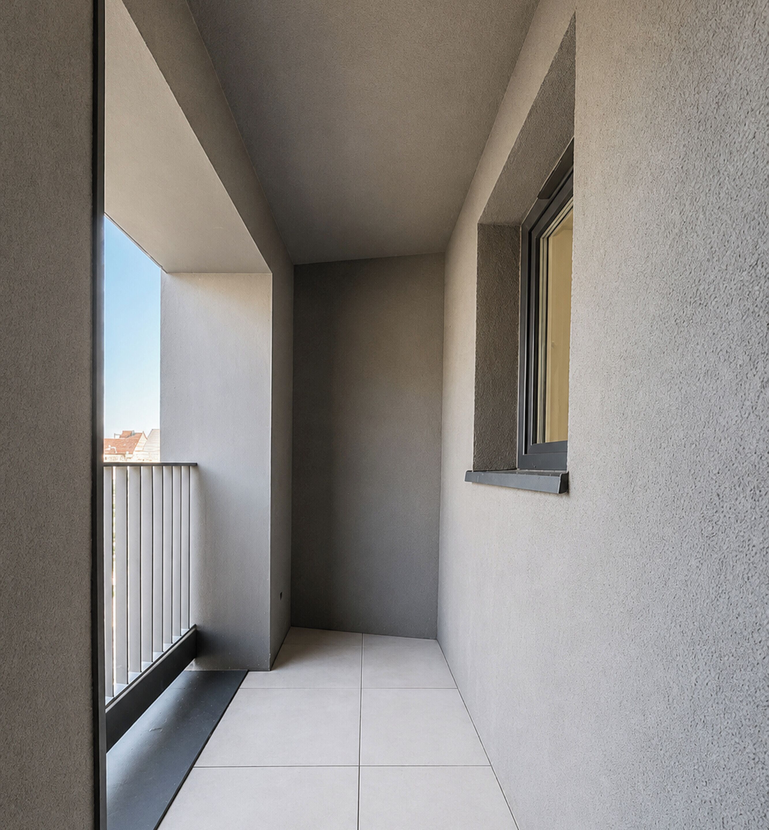 Een smalle gang met een raam aan de rechterkant en een balkon aan de linkerkant.