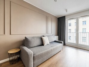En moderne stue med en grå sofa, et rundt sofabord og et stort vindue med udsigt til bygninger.