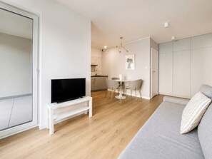 A modern living room with a flat-screen TV on a stand, a grey sofa, and a dining area with a table and chairs. - Sikorskiego Serene Apartment (Poznań)