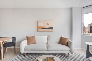 A modern living room with a sofa, a dining table, and a view of the city. - Blueground | Manhattan, rooftop, nr Empire State (New York)