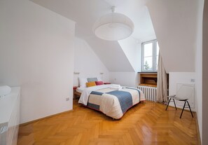 A bedroom with a sloped ceiling, a bed with a quilt, a chair, and a window. - Old Town Heritage Apartment (Warszawa)