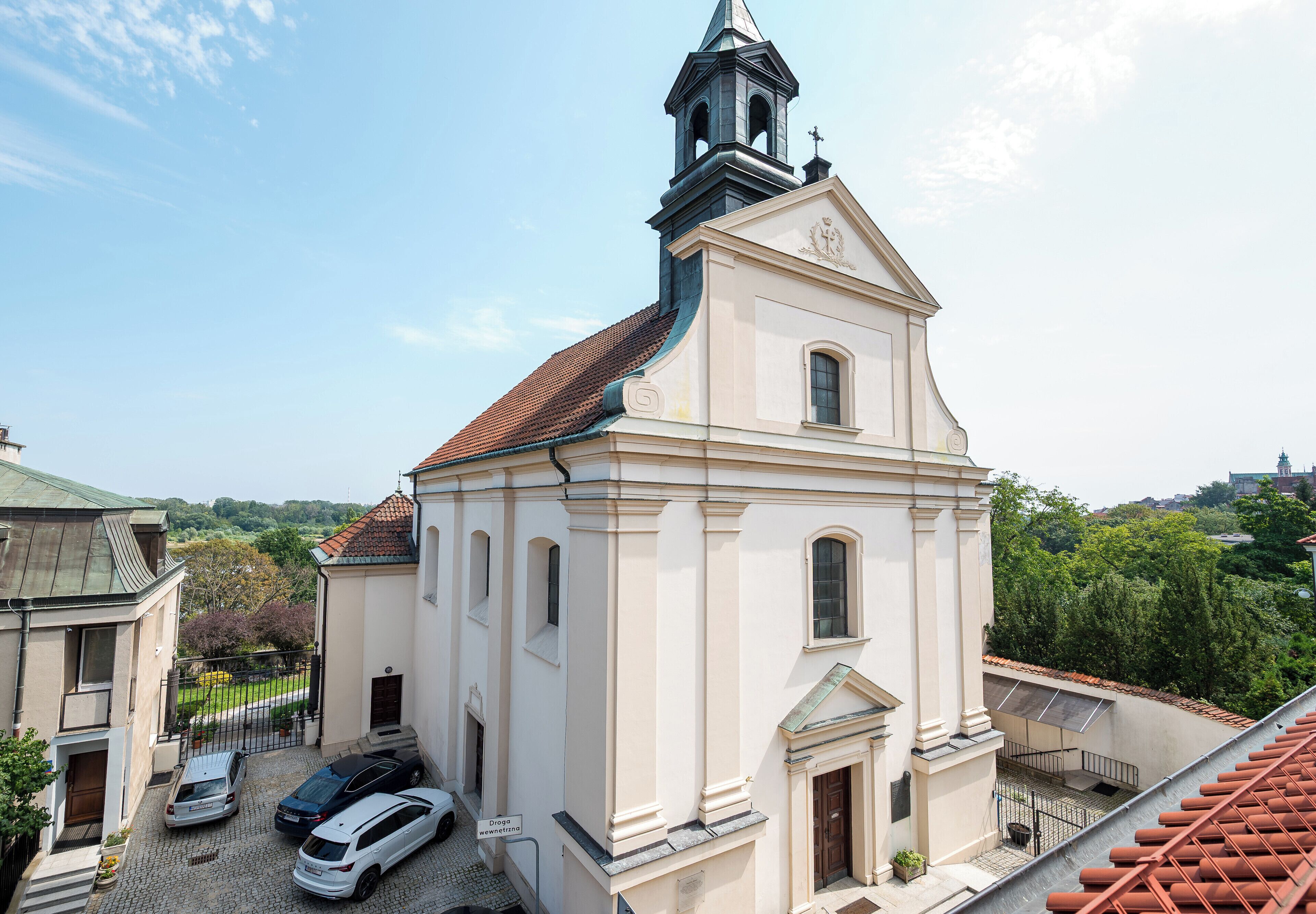 Una iglesia con un campanario, entrada empedrada y coches estacionados.