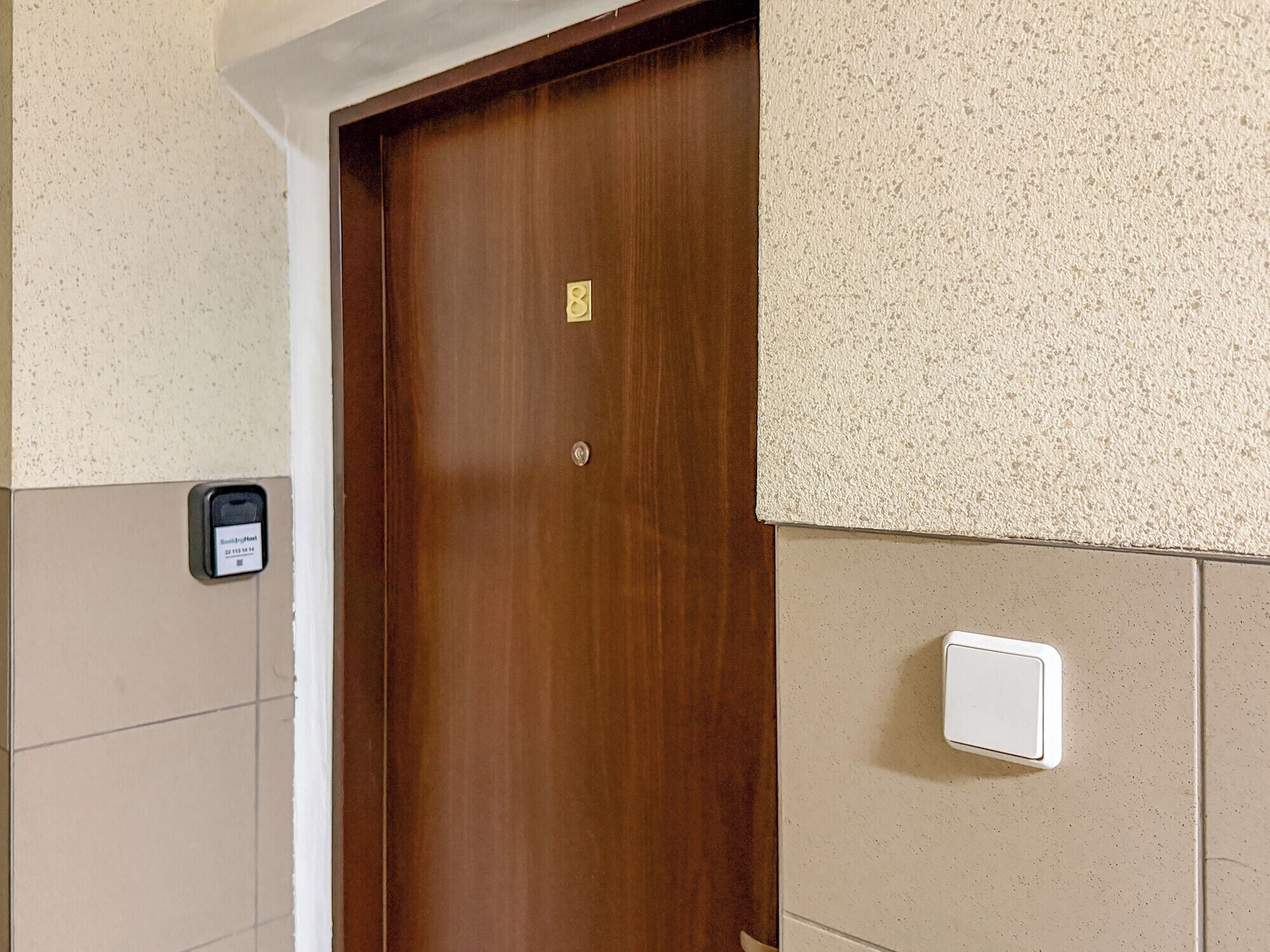 Une porte en bois avec une plaque de numéro, un interphone fixé au mur et un interrupteur.