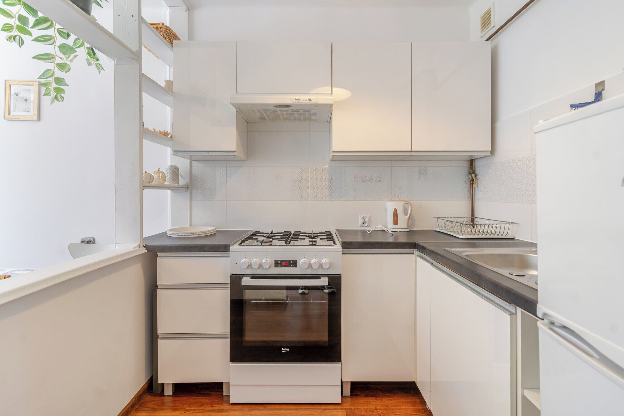 Une cuisine compacte avec des meubles blancs, une cuisinière à gaz, un four encastré et un évier en acier inoxydable.