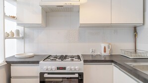 Una cocina moderna con armarios blancos, estufa a gas, horno empotrado y tetera sobre la encimera.