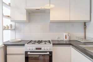Eine moderne Küche mit weißen Schränken, einem Gasherd, einem Backofen und einem Wasserkocher auf der Arbeitsfläche.