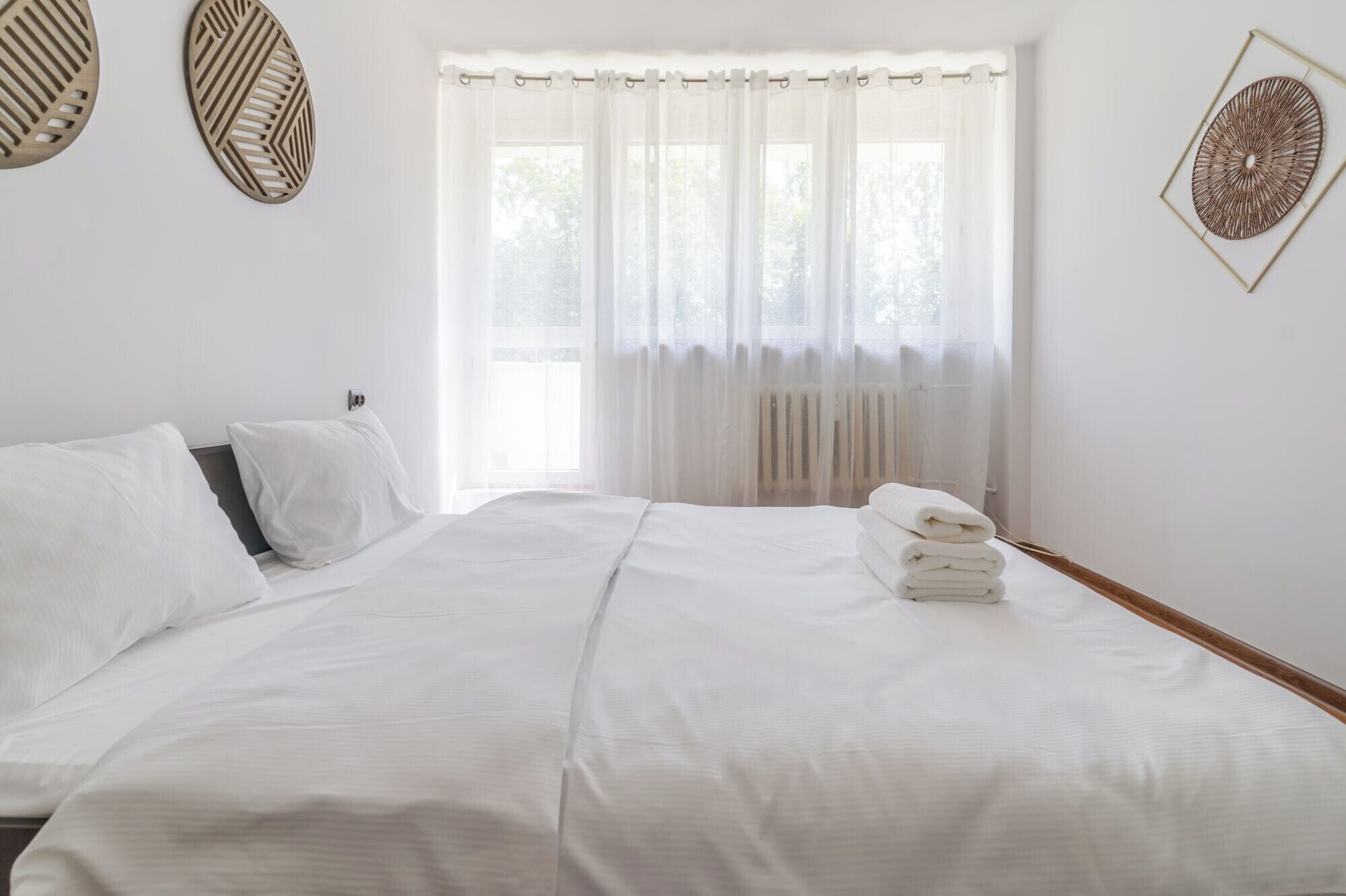 Une chambre d’hôtel avec un lit, une fenêtre avec des rideaux légers et un radiateur.