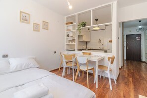 A compact living space with a kitchenette, a dining area with a table and chairs, and a bed. - Park Śląski Bright Apartment (Katowice)