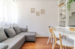 A modern living room with a grey sectional sofa, a dining table with chairs, and a white cabinet with shelves. - Park Śląski Bright Apartment (Katowice)
