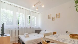 Un dormitorio con cama, escritorio, silla, mesa y ventana con cortinas.