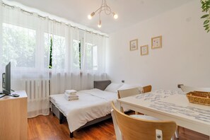 Ein Schlafzimmer mit Bett, Schreibtisch, Stuhl, Tisch und einem fenster mit Vorhängen.