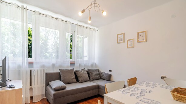 Una habitación acogedora con un sofá gris, una mesa de comedor de madera con sillas, y un televisor sobre un escritorio.