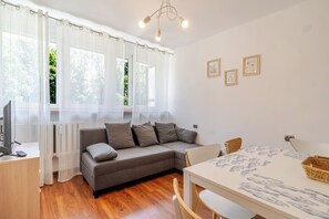 A cozy room with a grey sofa, a wooden dining table with chairs, and a TV on a desk. - Park Śląski Bright Apartment (Katowice)