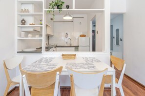 A dining area with a white table and chairs, a hanging plant, and a view into a kitchen with white cabinets and a stove. - Park Śląski Bright Apartment (Katowice)