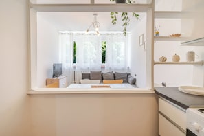 A modern kitchen with white cabinetry, a dining area with a table and chairs, and a window with sheer curtains. - Park Śląski Bright Apartment (Katowice)