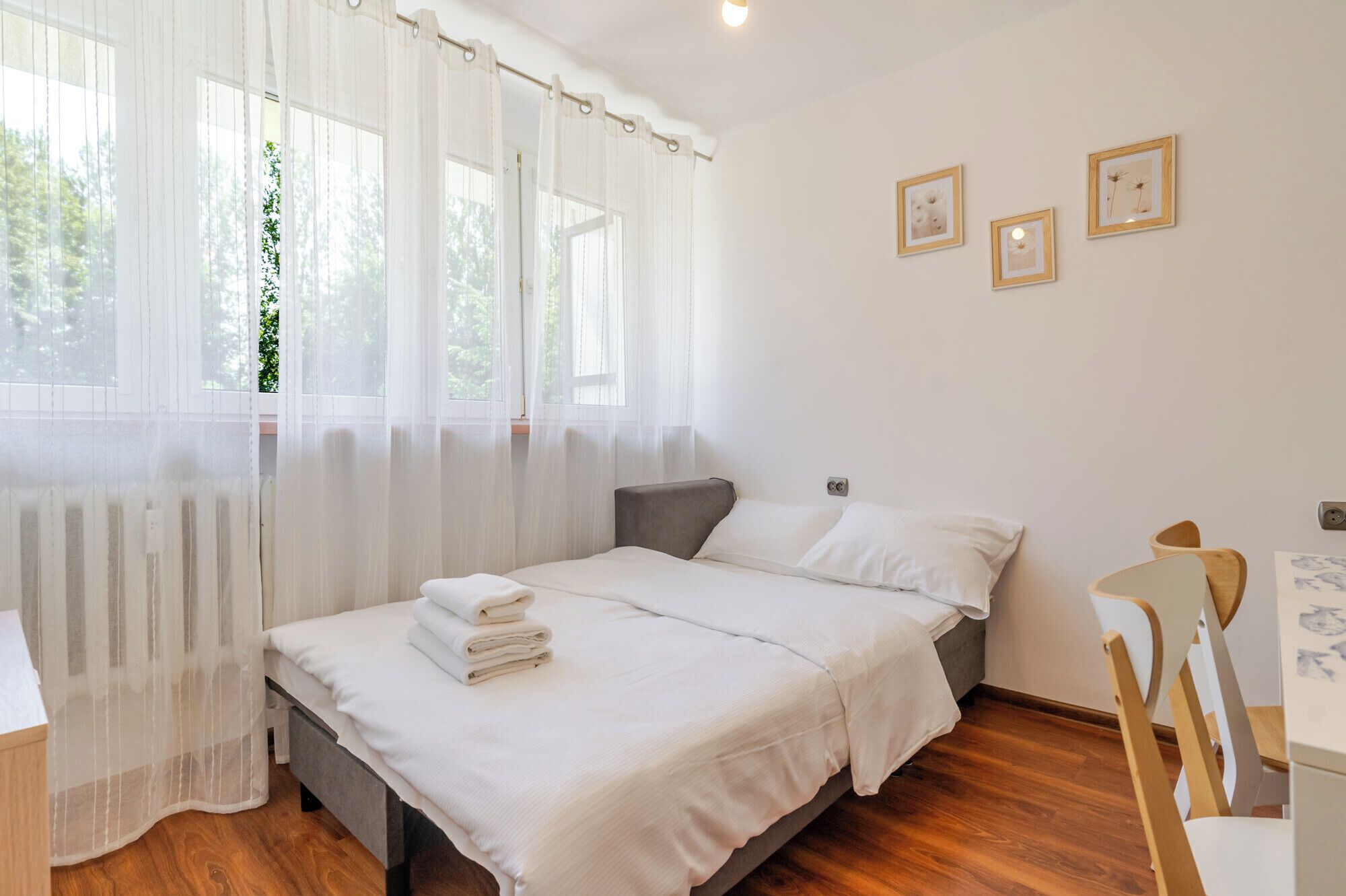 Un dormitorio con cama, una silla, una mesa y una ventana con cortinas.