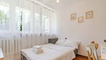Un dormitorio con cama, una silla, una mesa y una ventana con cortinas.