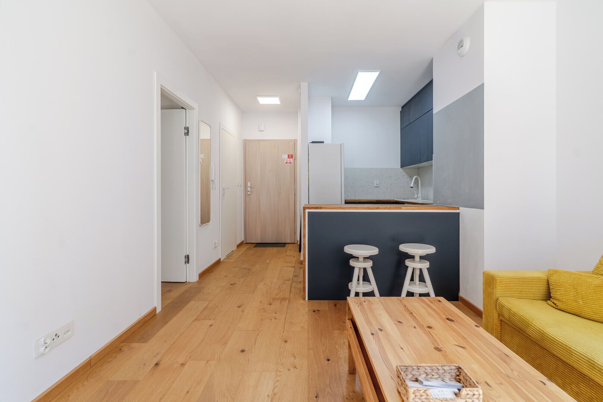 Una cocina moderna con encimera de madera, dos taburetes y un sofá amarillo.