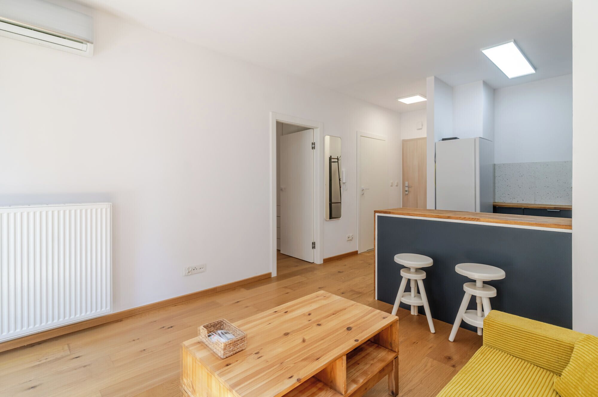A modern living space with a wooden floor, a kitchen area with a fridge, and a dining area with stools.