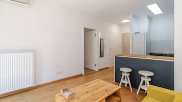 A modern living space with a wooden floor, a kitchen area with a fridge, and a dining area with stools.