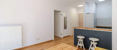 Un espace de vie moderne doté d’un plancher en bois, d’un coin cuisine avec réfrigérateur et d’un coin repas avec des tabourets.