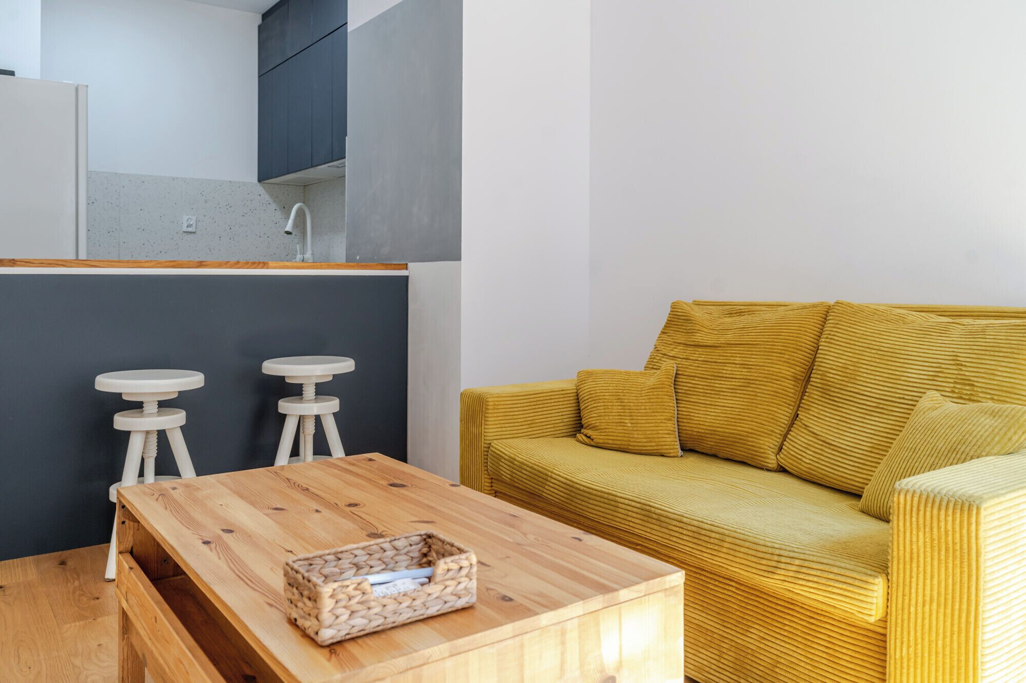 A compact living space with a wooden coffee table, a yellow sofa, and two white stools.