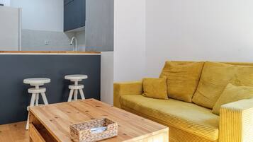 A compact living space with a wooden coffee table, a yellow sofa, and two white stools.