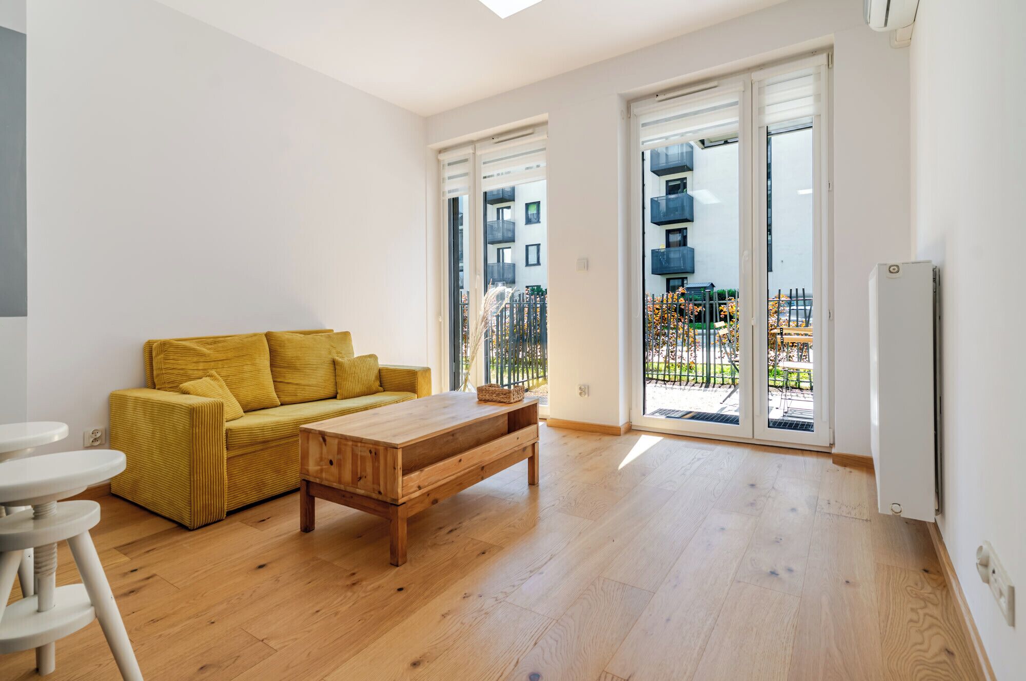 A modern living room with a yellow sofa, a wooden coffee table, and a sliding glass door leading to a balcony.